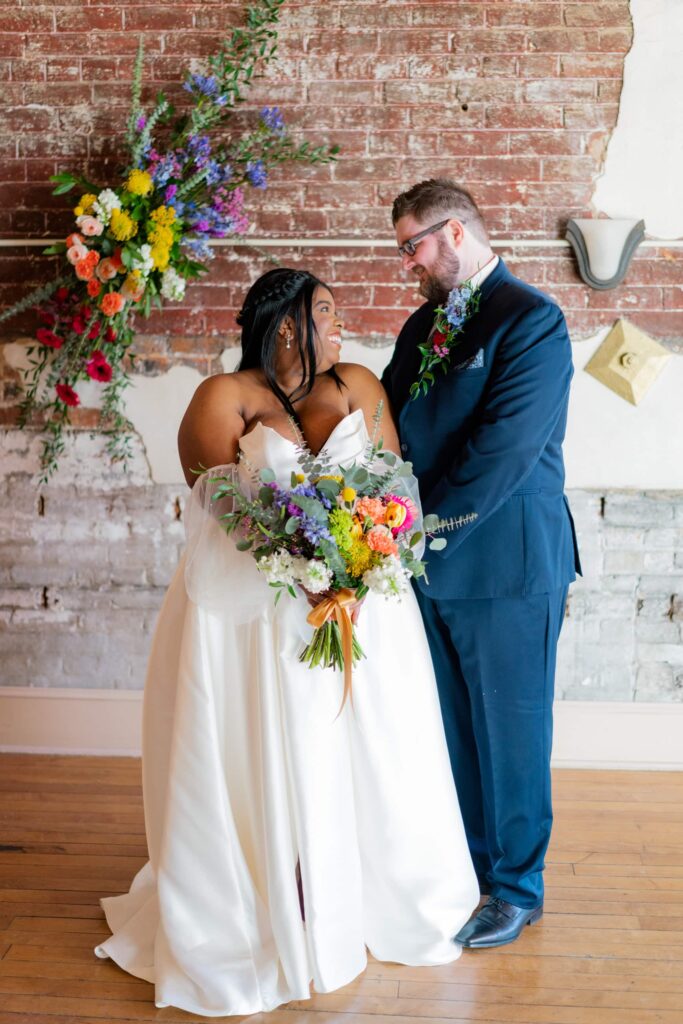 Wedding portrait with rainbow themed flowers at American Hotel in downtown Staunton Virginia, taken up against the exposed brick wall